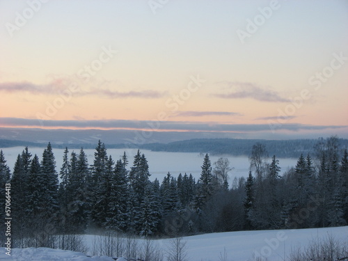 A winter sunset landscape is a breathtaking sight as the warm hues of the setting sun create a contrast against the cold, frosty mist that settles over the ground.