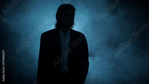 Shot of a young assassin with long hair. A young hitman with long hair coming from the darkness and shooting bullets, Cinematic light, and some smoke. HD footage 24 FPS. photo