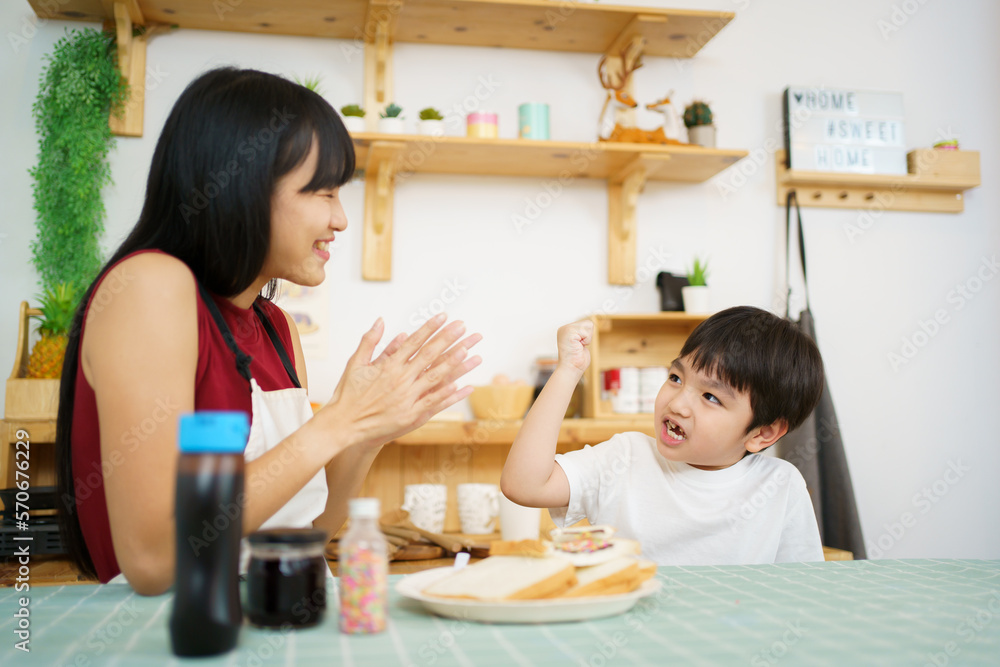 Happy little young boy and his mother making an easy breakfast together in a kitchen with a breads and chocolate jam. Mother and son playing together while making a breakfast. Happy little young boy and his mother making an easy breakfast together in a kitchen with a breads and chocolate jam. Mother and son playing together while making a breakfast.