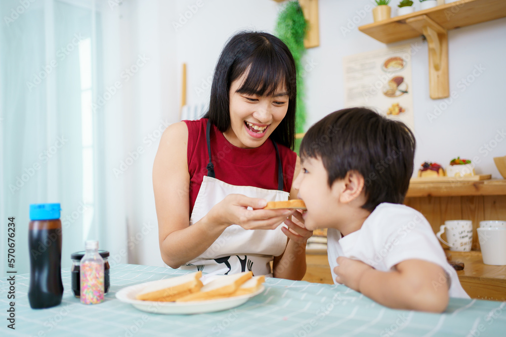 Happy little young boy and his mother making an easy breakfast together in a kitchen with a breads and chocolate jam. Mother and son playing together while making a breakfast. Happy little young boy and his mother making an easy breakfast together in a kitchen with a breads and chocolate jam. Mother and son playing together while making a breakfast.