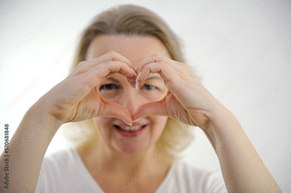 middle-aged woman makes hands as if glasses in front of eyes showing heart with hands looks through hole smiles love expectations recognition tenderness beauty hands in sharpness selective sharpness middle-aged woman makes hands as if glasses in front of eyes showing heart with hands looks through hole smiles love expectations recognition tenderness beauty hands in sharpness selective sharpness