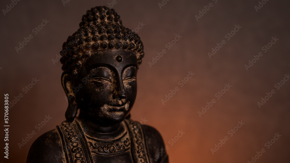 Statue of Buddha close-up in a dark environment with golden background illuminated by candlelight. Empty space for text on the right