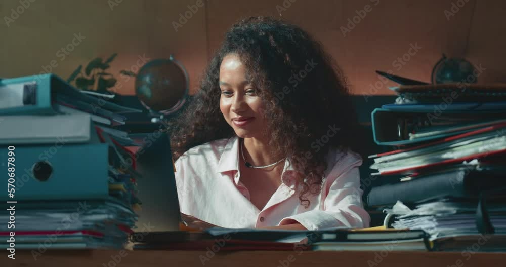 Happy busy young mixed race female boss, accounting manager smiles working at home table surrounded by many documents. Happy busy young mixed race female boss, accounting manager smiles working at home table surrounded by many documents.
