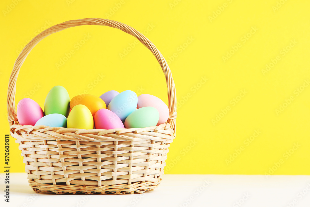 Different colorful easter eggs in basket on yellow background