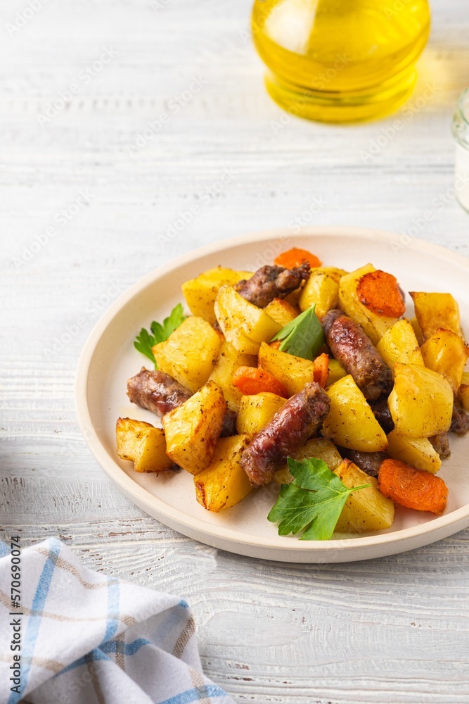 Sliced baked potatoes, carrots and sausages on a ceramic plate on a light wooden background Sliced baked potatoes, carrots and sausages on a ceramic plate on a light wooden background