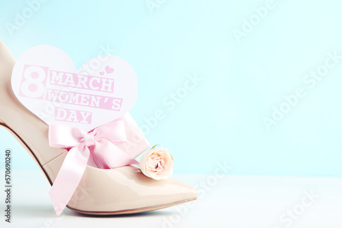 Flower of rose, gift and card in shape of with text 8 March Women's Day, and beige high-heeled shoe on blue background
