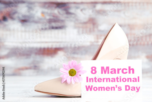 Flower of chrysanthemum, card with text 8 March International Women's Day and beige high-heeled shoe on wooden background