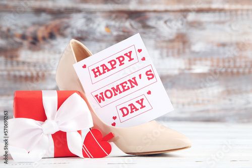 Card with text Happy Women's Day, gift and beige high-heeled shoe on wooden background