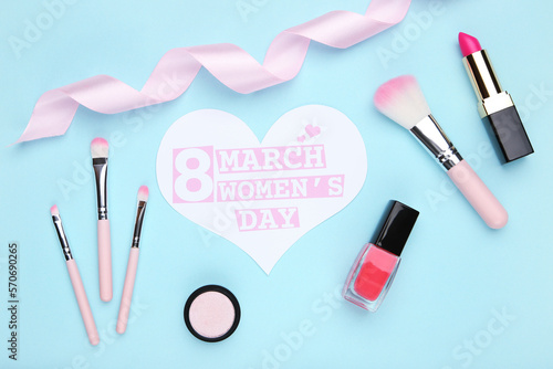 Card in shape of heart with text 8 March Women's Day, ribbon, makeup brush set, nail polish and lipstick on blue background