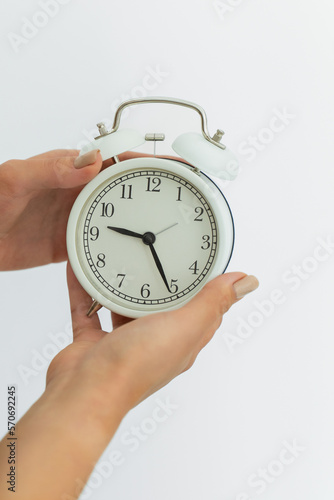 Female hands holding an alarm clock on a white background