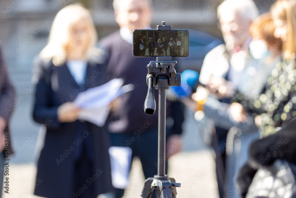 Filming whistleblower holding confidential document at media event or news conference with smartphone. Mobile or citizen journalism concept.