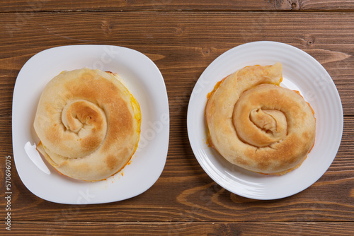 Two ready-made golden sweet cakes, lie on white plates, on a wooden table photo