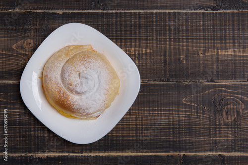 Ready-made vertuta with pumpkin lies on a white plate, sprinkled with powdered sugar, on a wooden table, flat lay photo