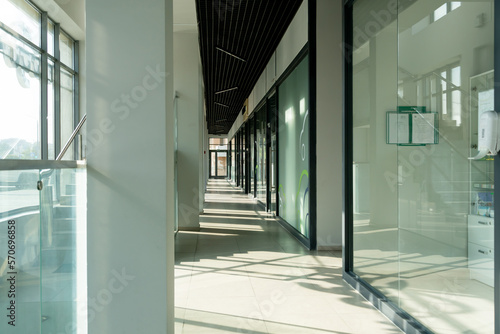 A corridor in an urban-type office building. Modern interior of the lobby of an office building with glass doors, walls and large spacious windows. A lighted long corridor in a modern business center