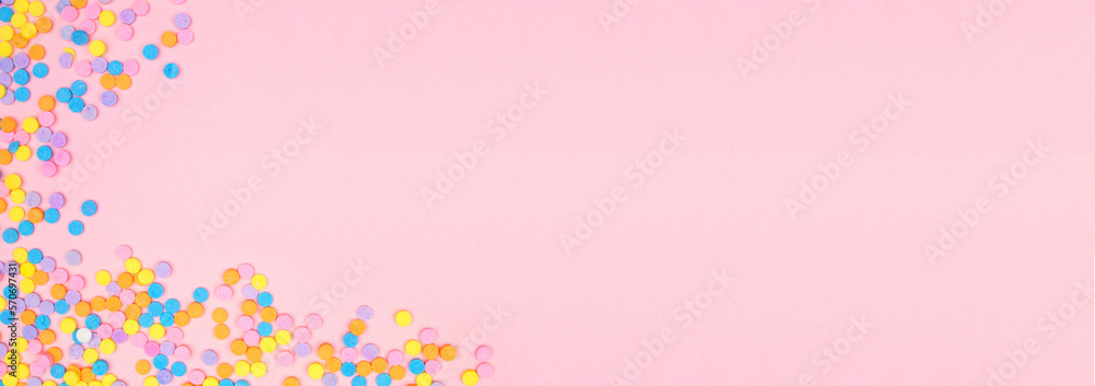 Colorful candy sprinkles corner border. Top down view banner on a pink background. Pastel color theme. Copy space.