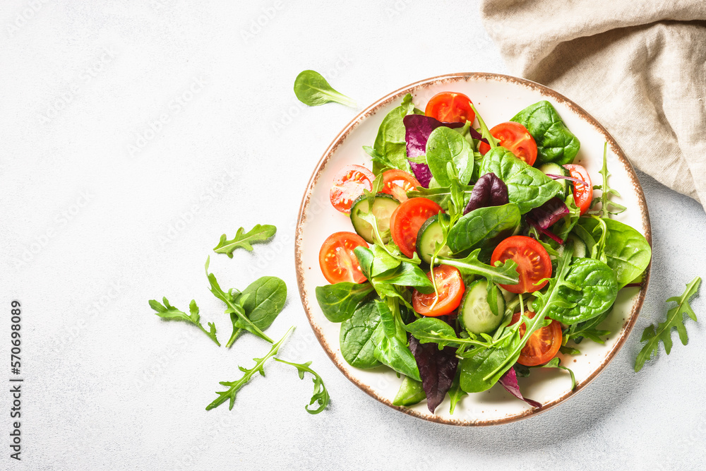 Green salad with fresh leaves and vegetables in white plate. Top view.
