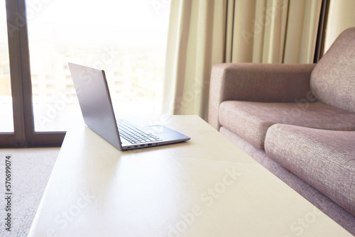 Personal laptop computer is open on a wooden table. Living room. Nobody. Empty space for design. Workplace. Modern interior. Sofa.Window.Freelance, remote work, learning, studying concept. Beige color © Наталья Босяк
