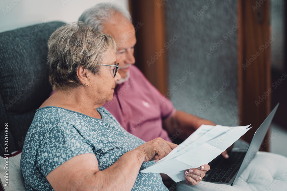 Φωτογραφία SIde view of real senior couple at home paying bills online with internet banking app and account