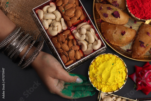 A woman girl lady with beautiful bangles arranging Abeer gulal dry color powder and Indian sweet Gujiya pedukiya kashew for the celebration of Holi festival of colors photo