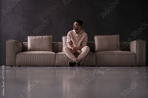 Stylish African American man wearing black framed glasses on a sofa in minimalistic interior