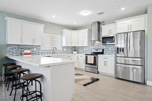 White Coastal kitchen with stainless steel appliances and sea glass backsplash tile. 