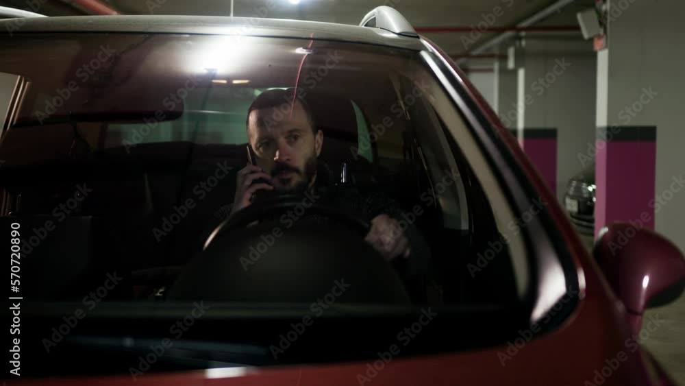 Brunette man talking on the phone and holding car wheel. Driver making a call at the parking lot. Busy guy using smartphone in his automobile Brunette man talking on the phone and holding car wheel. Driver making a call at the parking lot. Busy guy using smartphone in his automobile