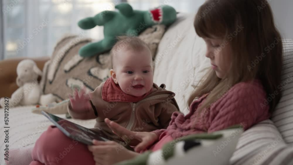 Two Little Baby Girls Sitting on the Couch and Use Digital Tablet Computer Two Little Baby Girls Sitting on the Couch and Use Digital Tablet Computer