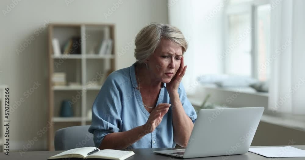 Older woman having blurry vision, eye-sight problems, put on glasses and working on laptop sit at desk, engrossed in job at home office. Advertises eyewear store and eyesight check up clinic services Older woman having blurry vision, eye-sight problems, put on glasses and working on laptop sit at desk, engrossed in job at home office. Advertises eyewear store and eyesight check up clinic services