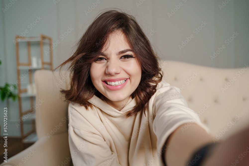 Pretty young female with big smile sitting at living room. She having fun taking selfie. Pretty young female with big smile sitting at living room. She having fun taking selfie.
