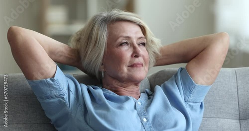 Carefree senior pretty woman smile, relax on cozy sofa, take break, breath fresh conditioned air inside warm living room, put hands behind head enjoy untroubled retired life, close up. Daydreams, rest