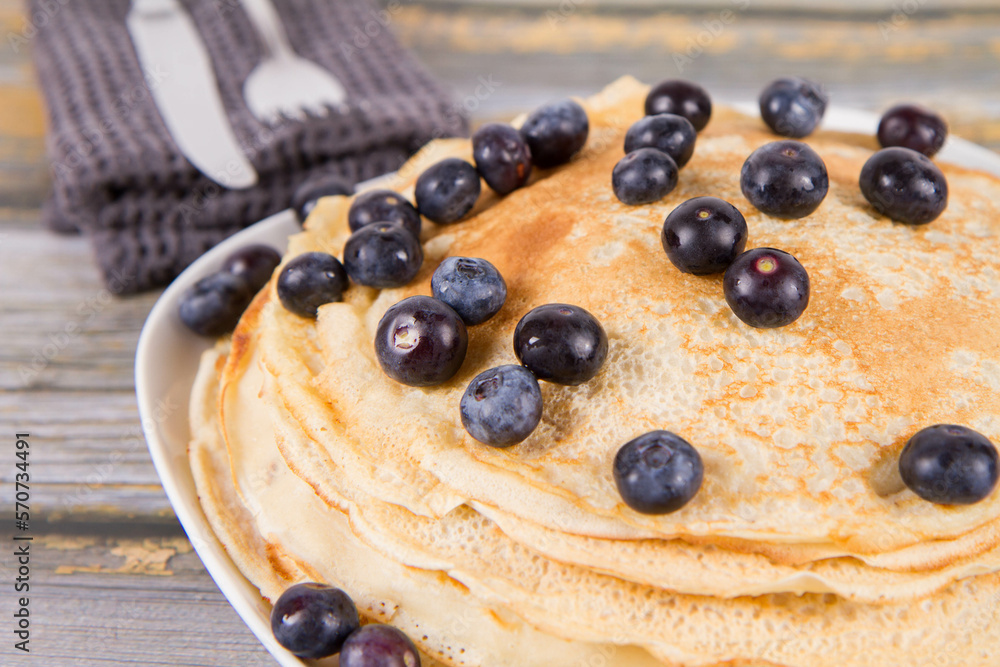 Pile of crepes with blueberry fruit on a wooden background