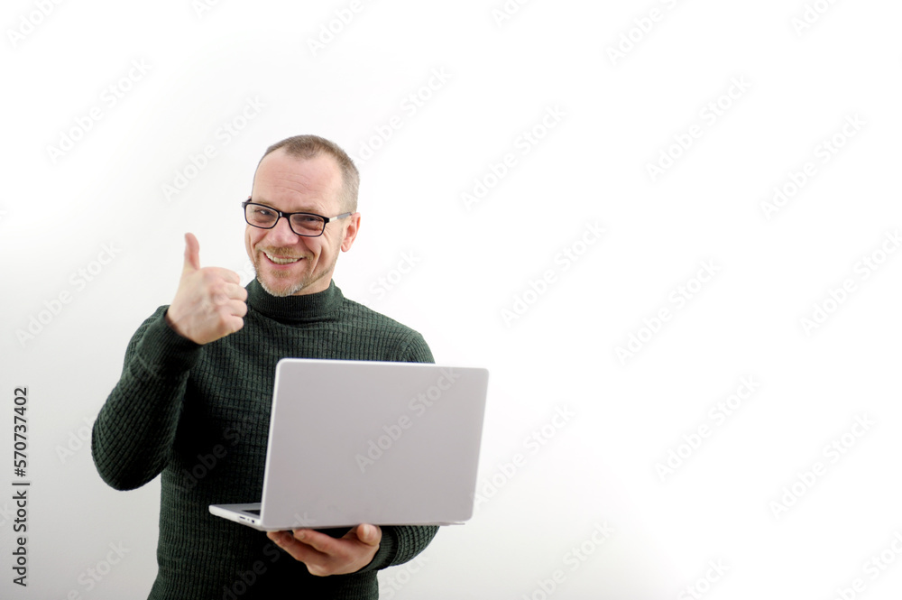adult man in glasses with a beard and a mustache is very happy he shows a thumbs up in his hands he has a gray laptop on a white background 50-60 years old green sweater good luck success victory adult man in glasses with a beard and a mustache is very happy he shows a thumbs up in his hands he has a gray laptop on a white background 50-60 years old green sweater good luck success victory