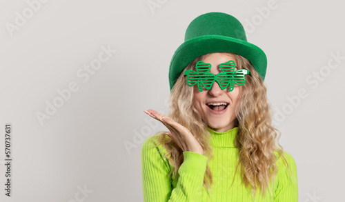 St. Patrick's Day leprechaun surprised model woman in green hat, funny clover shaped sunglasses, isolated on white background and smiling, having fun. Patrick Day party, wow face.