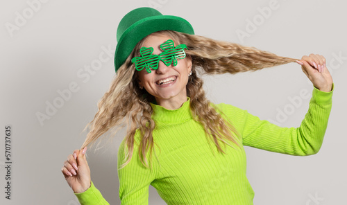 St. Patrick's Day leprechaun surprised model woman in green hat, funny clover shaped sunglasses, isolated on white background and smiling, having fun. Patrick Day party, wow face.
