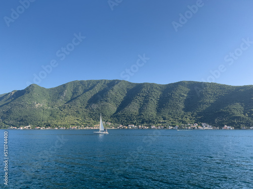 Sailboat sails along the sea near the mountain coast against the backdrop of a clear blue sky