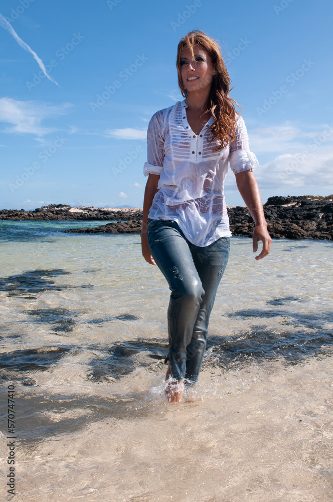 Wet young woman in clothes on the seashore in spring or summer under a blue sky Wet young woman in clothes on the seashore in spring or summer under a blue sky