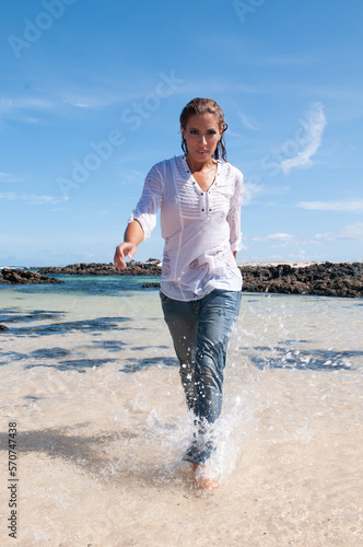 Wet young woman in clothes on the seashore in spring or summer under a blue sky