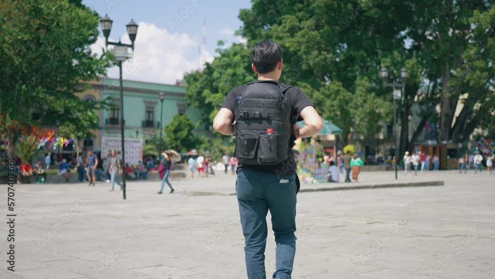 Slow motion male traveler walking outside old cathedral, zoom in pan around view of Hispanic men with sunglasses and backpack on sunny day in Oaxaca, Mexico Slow motion male traveler walking outside old cathedral, zoom in pan around view of Hispanic men with sunglasses and backpack on sunny day in Oaxaca, Mexico