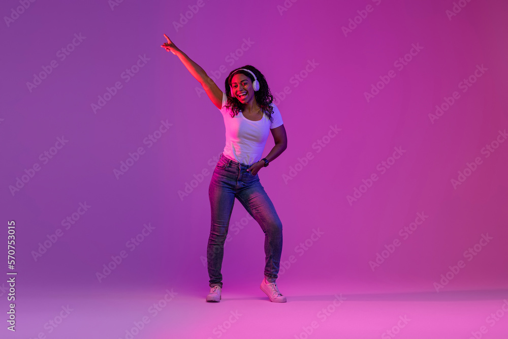 Joyful Black Woman Wearing Wireless Headphones Having Fun In Neon Light
