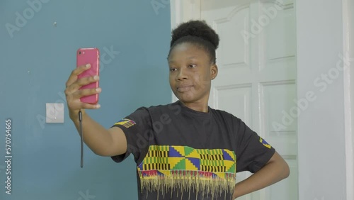 A young black woman in a Kente T-Shirt takes a selfie photo