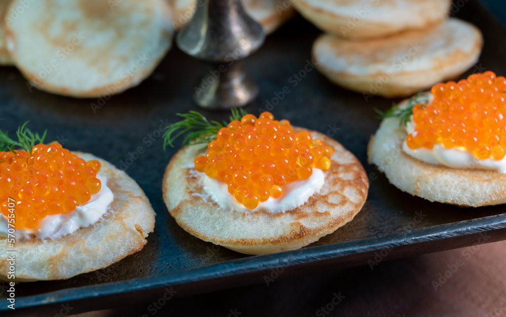 Tasty appetizer for dinner, small pancakes bliny with red fish caviar and sour cream Tasty appetizer for dinner, small pancakes bliny with red fish caviar and sour cream