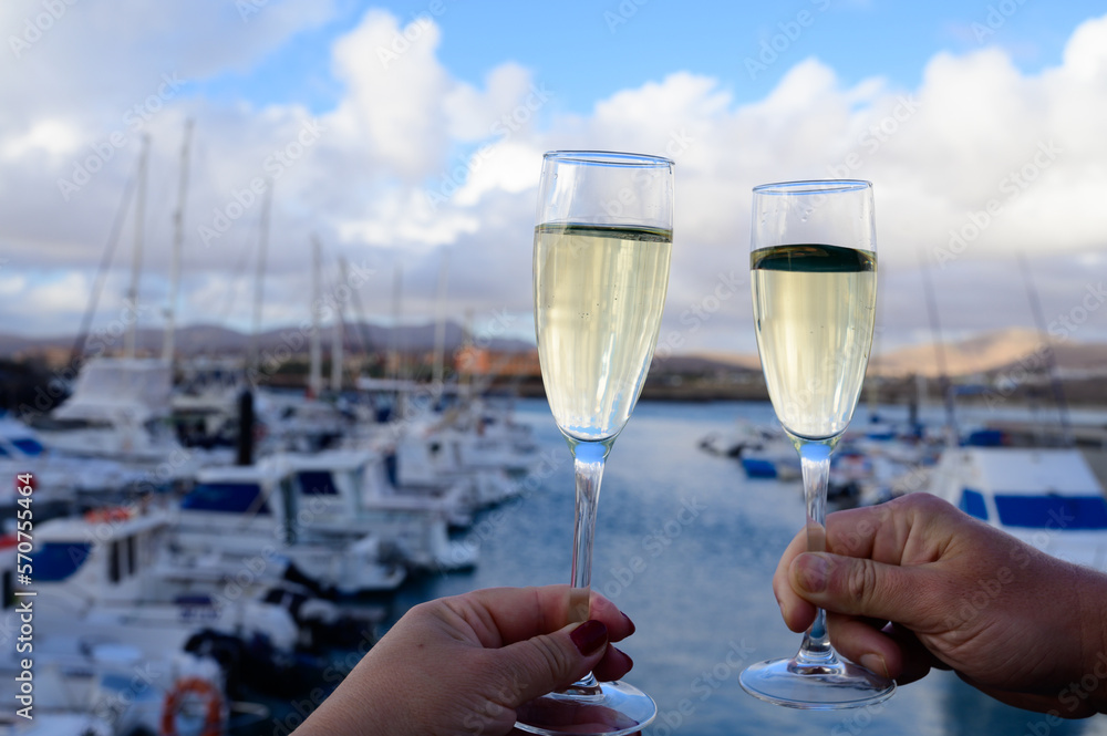 Obraz premium Everyday party, hands with glasses of cava or champagne sparkling wine in yacht harbour of Caleta Fuste, Fuerteventura, Canary islands vacation, Spain