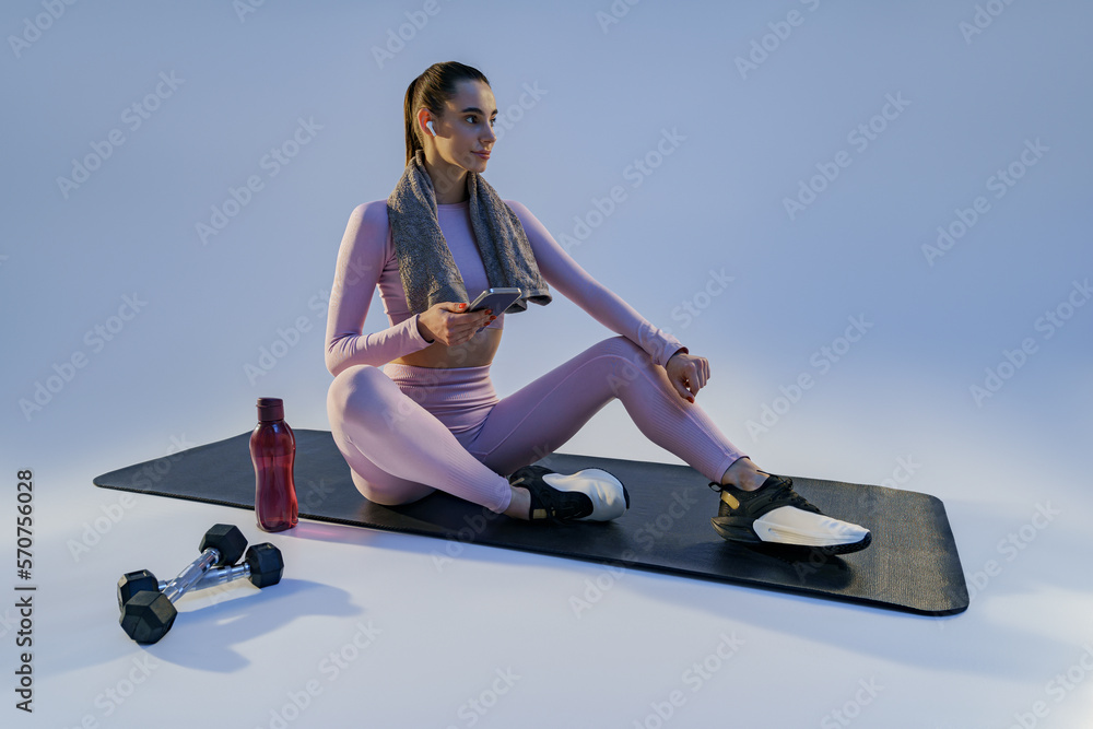 Woman resting after training with smartphone sitting on studio background. High quality photo
