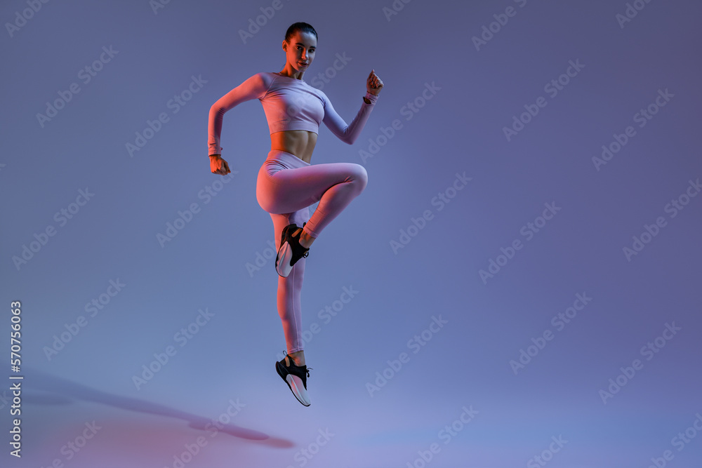 Athletic active woman jumping on studio background with colored filter. Dynamic movement