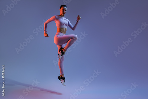 Fototapeta Naklejka Na Ścianę i Meble -  Athletic active woman jumping on studio background with colored filter. Dynamic movement