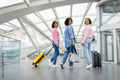 Three Beautiful Women Walking With Luggage At Airport And Turning At Camera