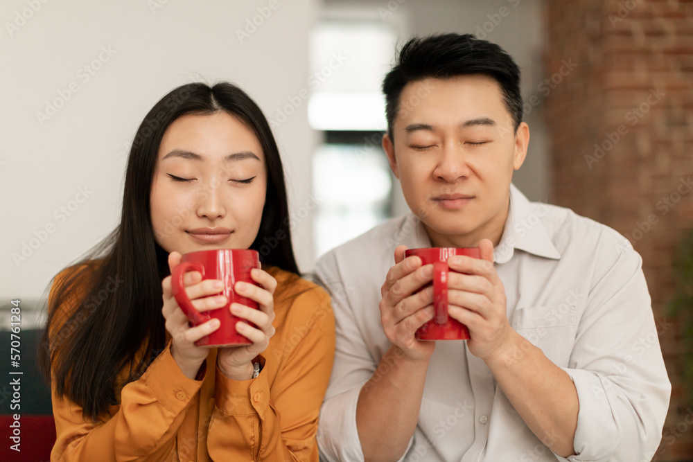 Calm asian young woman and middle aged man smelling fresh aromatic morning coffee with closed eyes Calm asian young woman and middle aged man smelling fresh aromatic morning coffee with closed eyes