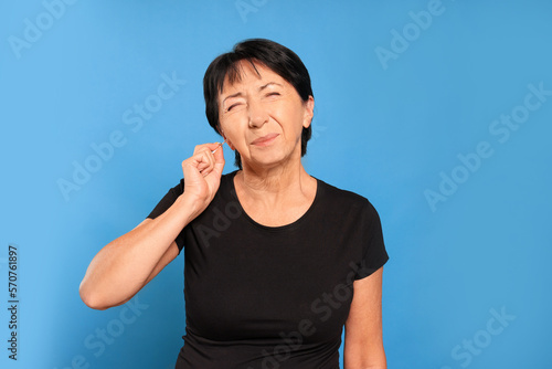Senior woman cleaning ear with cotton swab on light blue background