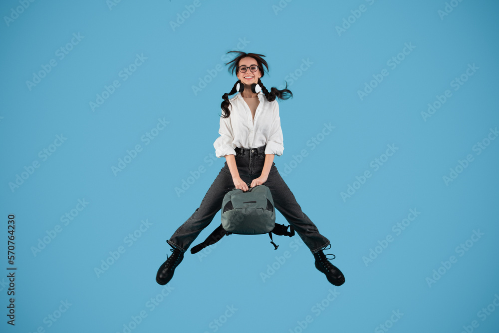 Happy caucasian teenager girl with pigtails in glasses with headphones student jumping, freezes in air Happy caucasian teenager girl with pigtails in glasses with headphones student jumping, freezes in air