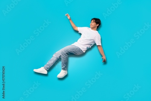 Asian Teenager Boy Falling In Mid Air Over Blue Background